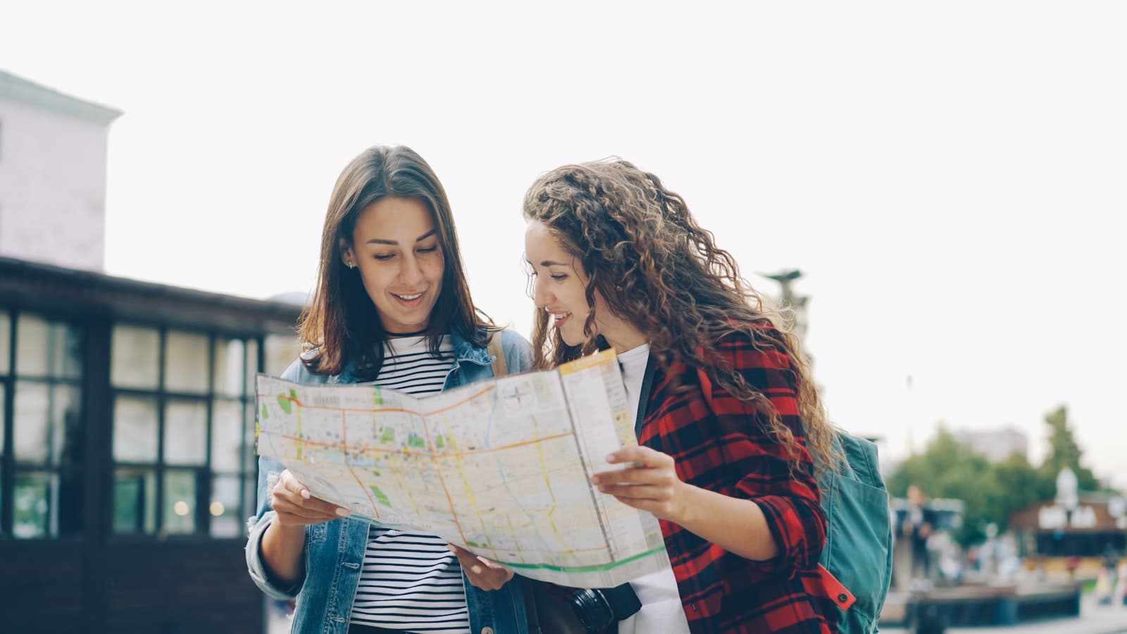 Two women comparing routes on a paper map while exploring a city
